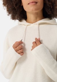 Helle, cremefarbene Kapuzenjacke mit gerippter Textur, langen Ärmeln und Kordelzug-Details. Hat einen übergroßen Schnitt und weite Bündchen.