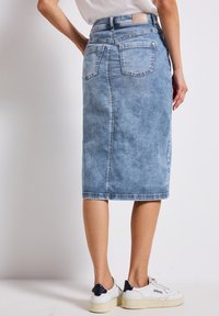 Keskiviimevöi denim midi-hame heledas sinises, sobiva vöökohaga, tagakotidega ja toore äärega. Kombineeritud valgete tossudega, millel on tumesinine aktsent.