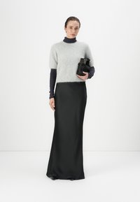 Grijze mohairmix sweater met korte mouwen, gelaagd over een donkere coltrui, gecombineerd met een lange zwarte satijnen rok en een zwarte tas.
