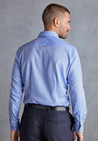 Blauw schotse ruitpatroon shirt met lange mouwen, knoopmanchetten en een getailleerd ontwerp. Gepaard met donkere broeken en een zwarte riem.