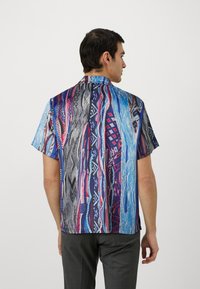 Short-sleeve shirt featuring a vibrant abstract pattern in blue, pink, and black. Soft fabric with a relaxed fit and classic collar.