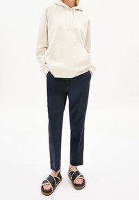 Persona vestida con una sudadera color crema, pantalones navy a medida con aberturas frontales y sandalias negras con suelas de madera gruesas y tiras de borreguito.