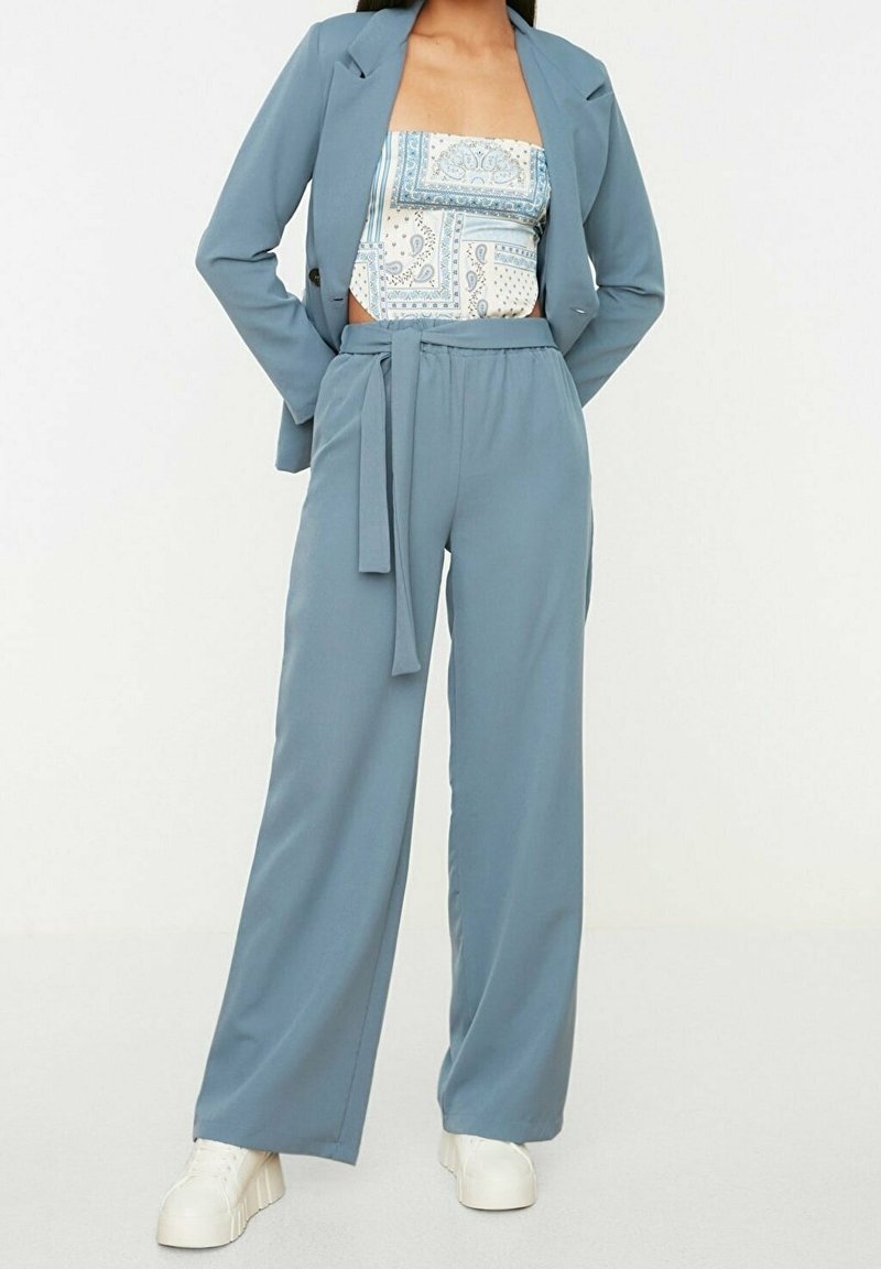 Svetle modrý oblek na míru s širokými kalhotami. Vrchní část má bílo-modrý vzorovaný bandeau. Hladká tkanina a detail s opaskem.