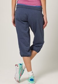 Temně modré kapri tepláky s elastickými manžetami a měkkým pasem, spojené s barevnými sportovními botami s puntíkovým vzorem.