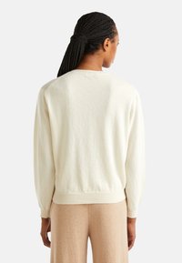 Maglione color crema con un tessuto morbido e testurizzato, vestibilità rilassata, spalle cadenti e polsini e orlo a coste. Visuale da dietro.