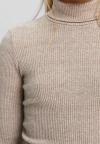 Beżowy sweter z golfem o prążkowanej strukturze, wykonany z miękkiego materiału, z dopasowanym krojem i subtelną teksturą, sięgający do szyi.
