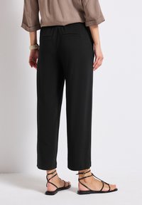 Black, wide-leg pants with an elastic waistband, featuring two back pockets. Paired with black flat sandals with thin straps.