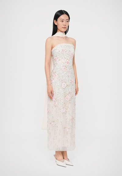 Suknia bez ramiączek z przezroczystej, lekkiej tkaniny z różowo-niebieskim kwiatowym haftem, sięgająca do podłogi, w komplecie z białymi butami na szpic.