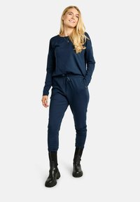 Súprava domáceho oblečenia tmavomodrej farby z mäkkej látky, pozostávajúca z trička s dlhým rukávom a nohavíc so šnúrkou v páse, doplnená čiernymi členkovými čižmami.