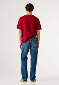Camiseta roja de algodón con mangas cortas, combinada con jeans de mezclilla azul de corte clásico y bolsillos traseros. Calzado casual completa el conjunto.