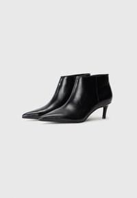 Bottines en cuir noir avec un bout pointu et un petit talon. Texture lisse et détails de couture minimaux visibles sur les côtés.