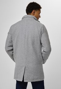 Manteau en mélange de laine gris avec un col montant, un motif en chevrons texturé et une fente dans le dos. Présente une coupe décontractée et des poches latérales.