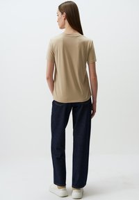 T-shirt beige a maniche corte con scollatura rotonda, abbinata a jeans blu scuro a gamba dritta e sneakers bianche. Design semplice e minimal.