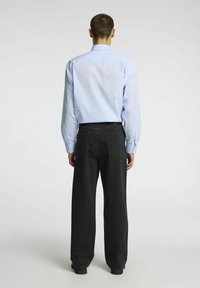 Light blue striped long-sleeve shirt with button cuffs, paired with wide-leg black jeans featuring pockets and a smooth finish.