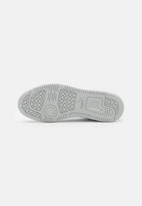 Semelle de chaussure en caoutchouc gris clair avec des motifs texturés, y compris des grips circulaires et des rainures horizontales pour la traction et le soutien.