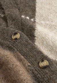 Close-up van gebreide wollen stof in bruin, beige en crème met twee ronde beige knopen genaaid op het gestructureerde kledingstuk.