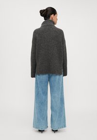 Maglione spesso grigio scuro a maglia con colletto alto, abbinato a jeans blu chiaro a gamba larga; design casual e testurizzato con dettagli a coste.