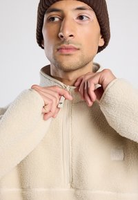 Pullover in pile beige chiaro con design a mezza zip, texture morbida, colletto a coste e dettaglio logo sottile sul petto.