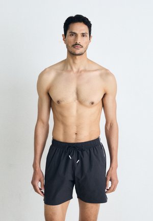 Zwarte zwembroek met een elastische tailleband en trekkoord, voorzien van witte zijkanten en een relaxte pasvorm. Geen andere details aanwezig.