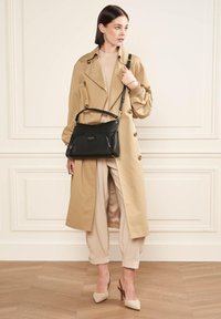 Mackintosh beige con grandi bottoni, borsa in pelle nera con dettagli dorati, top color crema e pantaloni chiari abbinati a tacchi beige.
