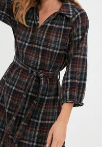 Kárované šaty v námořnické, burgundské a krémové barvě. Mají límeček, tříčtvrteční rukávy a zavazovací pas. Texturovaná tkanina s viditelným tkaním.