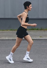 Mustan värvi spordibrassi, mustad jooksulühikesed, valged spordijalatsid mustade triipudega ja valged sokid. Teema jookseb asfaldipinnal.