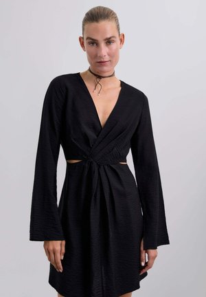 Black dress with long, bell sleeves, deep V-neck, and twisted waist detail. Made from textured fabric with cutout accents at the sides.