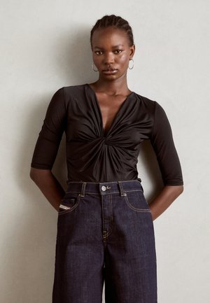 Svart tettsittende bodysuit med dyp utringning og tvistdetalj, kombinert med høyhalsede mørke denimbukser med kontrastsøm og lommer.