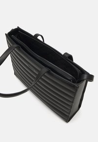 Černá kožená taška přes rameno s prošívaným designem, obsahující dvě ucha a zipové zapínání. Vnitřek je podšívkovaný hladkým materiálem.