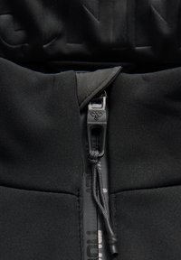 Veste noire zippée en tissu texturé. Comprend une fermeture éclair avant, un cordon réglable et un détail de logo imprimé sur le tissu.