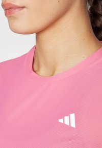 Maglietta atletica rosa in tessuto testurizzato, con colletto rotondo e un logo bianco sul lato sinistro vicino al colletto.