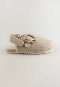 Chausson en feutre beige clair avec fermeture à boucle et doublure en fausse fourrure blanche. Dispose d'un bout arrondi et d'une semelle en caoutchouc texturé.