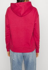 Fleece-hoodie i levende pink med foret hætte, ribbede manchetter og kant. Kombineret med lyse jeans med slidte detaljer.