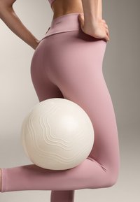 Rózsaszín, magas derekú leggings egy texturált, fehér fitneszgolyóval, amely a lábnak támaszkodik, sima, ívelt dizájnnal.