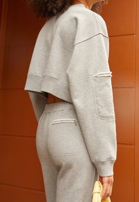 Grå kortärmad sweatshirt med raglan design, försedda med en ficka på ärmen och slitageeffekter. Matchas med gråa sweatpants.