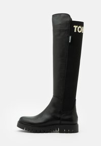 Mustat polvipituiset saappaat, joissa on nahkainen kärki ja joustava kangasvarsi. Pohjassa on rosoinen muotoilu, ja sivussa on huomattava logo.