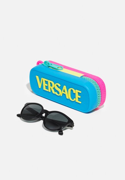 Mėlynas plastikinis saulės akinių dėklas su geltonu tekstu "VERSACE"; rožiniai ir geltoni akcentai. Juodi akiniai nuo saulės su apvalia katės akimis forma šalia dėklo.