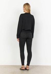 Zwarte lange mouwen top met een aansluitende taille, gecombineerd met donkere skinny jeans. Het model draagt gestreepte hoge hakken met een open achterkant.