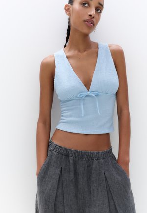 Lys blå cropped top med dyb v-hals og detaljer med frontknude, lavet af tekstureret stof; parret med grå, plisseret nederdel med elastisk talje.
