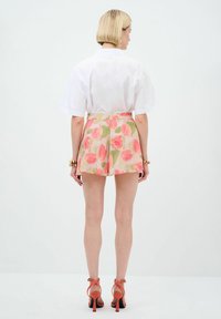 Pantaloni corti con un motivo floreale che presenta foglie rosa e verdi, abbinati a una camicia bianca con colletto e sandali con tacco arancioni.