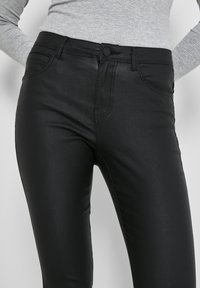 Pantalones ajustados negros hechos de un material suave y elástico. Presentan un botón en la parte delantera, dos bolsillos y un acabado elegante y pulido.
