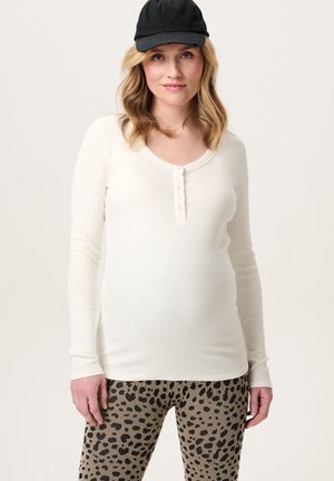 Weißes, ribbeltes Longsleeve-Oberteil mit weitem Rundhalsausschnitt und sechs Knöpfen, kombiniert mit taubefarbenen Leggings mit einem schwarzen Leopardenmuster.