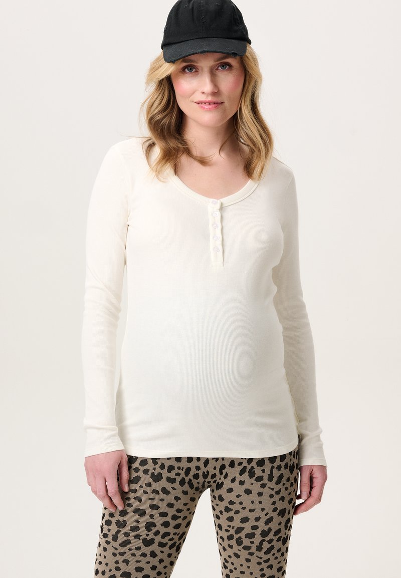 Weißes, ribbeltes Longsleeve-Oberteil mit weitem Rundhalsausschnitt und sechs Knöpfen, kombiniert mit taubefarbenen Leggings mit einem schwarzen Leopardenmuster.