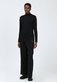 Schwarzes Langarm-Turtleneck-Oberteil, kombiniert mit locker sitzenden schwarzen Hosen. Minimalistisches Design mit dezentem Textdetail auf dem Oberteil.