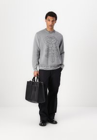 Gray sweater with floral design, textured hem, paired with black trousers and a sleek black tote bag. Smooth texture, casual fit.