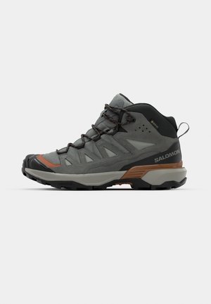 Hoge buitenschoenen in grijze mesh en suede, met een rubberen zool, vetersluiting en oranje accenten, ontworpen voor duurzaamheid en comfort.