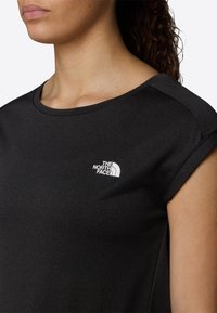 Černá, krátkozápěstní košile vyrobená z měkké tkaniny, s bílým logem na levé části hrudi a kulatým výstřihem.