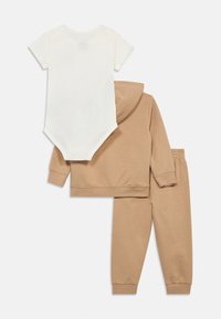 Béžová bavlnená mikina s kapucňou, zodpovedajúce nohavice a biele krátky rukáv body. Hladká textúra, elastický pás a dlhé rukávy na mikine.