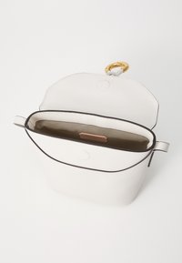 Hvit lærveske med en strukturert form, kontrasterende svart kanting, åpen topp og en gullring-detalj. Innvendig har den en beige foring.