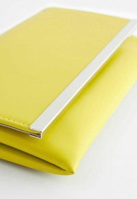 Pochette en cuir jaune avec un détail de barre métallique argentée élégante le long du bord du rabat sur fond blanc.
